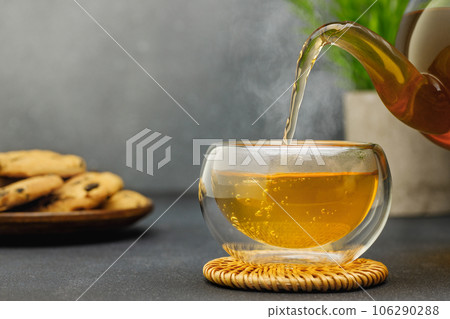 hot tea pouring from teapot into glass cup on table 106290288