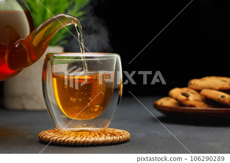 hot tea pouring from teapot into glass cup on table hot tea pouring from teapot into glass cup on table 106290289