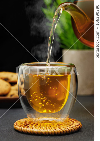 hot tea pouring from teapot into glass cup on table hot tea pouring from teapot into glass cup on table 106290290