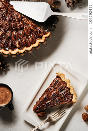 Traditional pecan pie, fall dessert concept for Thanksgiving. Top view on a tart with pecan nuts, coffee cup and piece pie on the plat Traditional pecan pie, fall dessert concept for Thanksgiving. Top view on a tart with pecan nuts, coffee cup and piece pie on the plat 106292452
