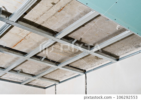 Metal frame on the ceiling for plasterboard installation in a commercial building, office or apartment. A simple and cheap way to renovate a room. Ceiling wiring of the electrical network. Metal frame on the ceiling for plasterboard installation in a commercial building, office or apartment. A simple and cheap way to renovate a room. Ceiling wiring of the electrical network. 106292553