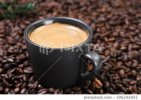 Realistic view of black espresso coffee in the dark cup in the roasted coffee beans. Cup with coffee crema and coffee beans.Close up and selective focus on the cup 106292841