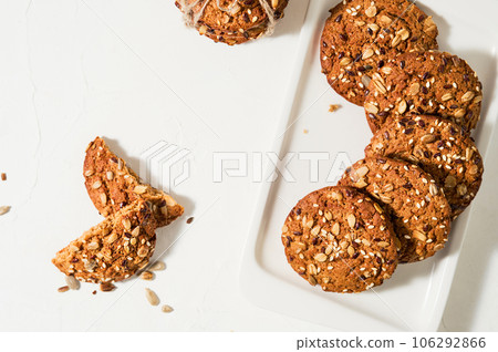 Homemade oatmeal cookies with flax and sesame seeds on a white table. Healthy food concept, breakfast snacks. Milk and biscuits. Healthy food still life. Layout of Christmas or New Year cookies. 106292866