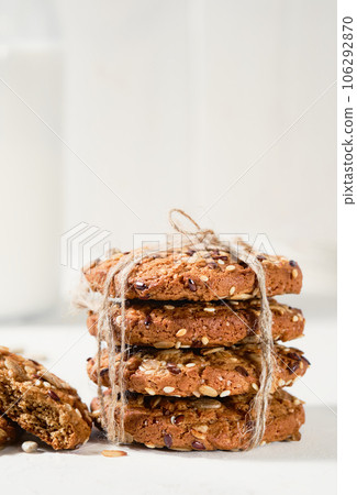 Oatmeal cookies with flax, sunflower and sesame seeds on a white table. Close-up selective focus on cookies. Healthy fitness food concept. Milk and craft biscuits for breakfast Oatmeal cookies with flax, sunflower and sesame seeds on a white table. Close-up selective focus on cookies. Healthy fitness food concept. Milk and craft biscuits for breakfast 106292870