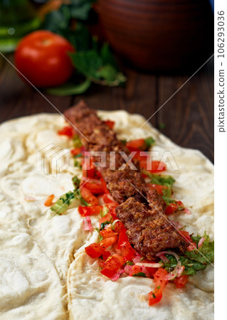Traditional oriental shish - adana kebab, shish kebab with tomatoes on pita bread with vegetables and spices. The process of cooking in the eatery. Turkish cuisine, close-up, shallow depth of field. Traditional oriental shish - adana kebab, shish kebab with tomatoes on pita bread with vegetables and spices. The process of cooking in the eatery. Turkish cuisine, close-up, shallow depth of field. 106293036