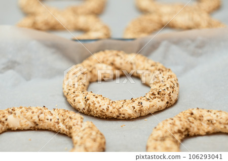 Simit prepared for baking on a baking sheet - a bun with sesame seeds close-up (Turkish bagel - Gevrek or Kuluri). Traditional white bread with sesame seeds for breakfast. 106293041