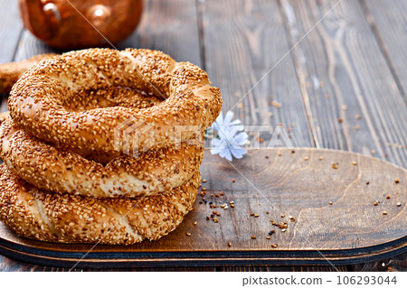 Freshly baked simit on a wooden table - sesame bun with copy space (Turkish bagel - gevrek or kuluri). Traditional white bread with sesame seeds for breakfast, next to a glass of tea. 106293044