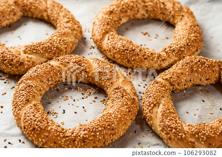 Freshly baked simit on a baking sheet - a close-up sesame bun (Turkish bagel - Gevrek or Kuluri). Traditional white bread with sesame seeds for breakfast. Freshly baked simit on a baking sheet - a close-up sesame bun (Turkish bagel - Gevrek or Kuluri). Traditional white bread with sesame seeds for breakfast. 106293082