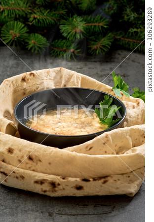 Traditional hot khash soup in a bowl, steam rises above the dish, close-up. Traditional Armenian, Caucasian oriental cuisine dish - khash, with fresh herbs, garlic and dried lavash bread Traditional hot khash soup in a bowl, steam rises above the dish, close-up. Traditional Armenian, Caucasian oriental cuisine dish - khash, with fresh herbs, garlic and dried lavash bread 106293289