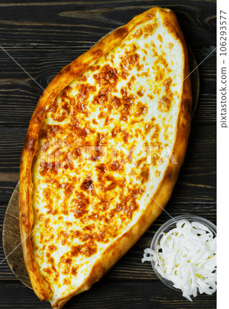 Turkish flatbread (pide) with cheese. Kasarli pide on the dark wooden table. Flat lay . Traditional turkish pizza Turkish flatbread (pide) with cheese. Kasarli pide on the dark wooden table. Flat lay . Traditional turkish pizza 106293577