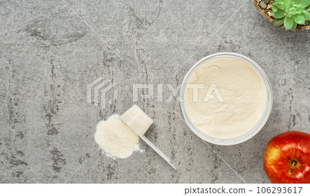 Collagen protein powder in a plastic measuring spoon and jar on a gray stone background, flat lay. Supplemental protein supplementation for body and joint health. On a natural basis. Space for text 106293617