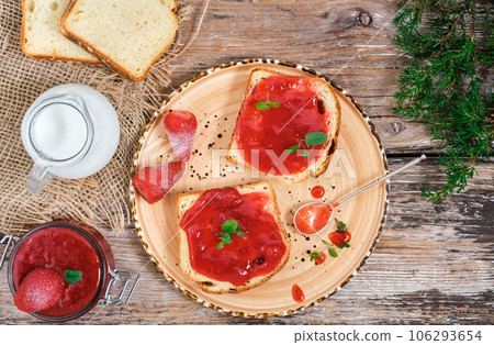 Fresh tasty strawberry jam on toast, decorated with mint leaves. Wooden rustic table. Sweet strawberry jam on the table, top view. Breakfast or lunch idea 106293654