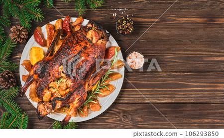 Festive Christmas duck baked with apples and quince and spices on dark vintage table. Festive dinner for Christmas or New Year. Cooking recipe, layout on wooden background decorated with fir branches 106293850