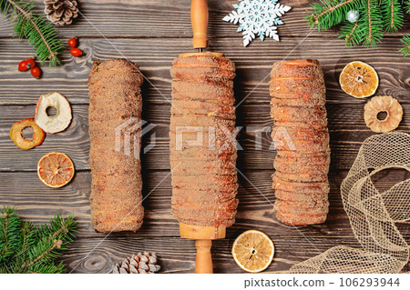 Delicacy from Trdelnik dough. Dough baked on a skewer and charcoal with sugar, cinnamon and vanilla. Christmas sweets, street food. Czech and Moravian cuisine. Delicacy from Trdelnik dough. Dough baked on a skewer and charcoal with sugar, cinnamon and vanilla. Christmas sweets, street food. Czech and Moravian cuisine. 106293944