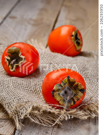Ripe delicious orange persimmons. Fresh persimmon on a matting mat, close-up. Wooden rustic table, vertical frame. Ripe delicious orange persimmons. Fresh persimmon on a matting mat, close-up. Wooden rustic table, vertical frame. 106293950