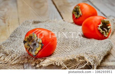 Ripe delicious orange persimmons. Fresh persimmon on a matting mat, close-up. Wooden rustic table, horizontal frame. 106293951