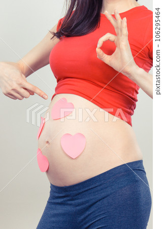 Woman in pregnant showing sign ok and pink hearts on her belly Woman in pregnant showing sign ok and pink hearts on her belly 106295464
