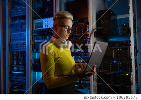 Side view of woman engineer working on laptop at network equipment 106295573