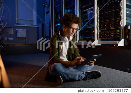 Teenager IT worker sitting on floor of modern server room working on tablet Teenager IT worker sitting on floor of modern server room working on tablet 106295577