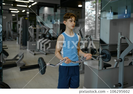 Strong teenager boy training himself exercising with barbell at gym club Strong teenager boy training himself exercising with barbell at gym club 106295602