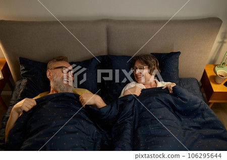 Happy laughing senior family couple in bed looking on each other Happy laughing senior family couple in bed looking on each other 106295644