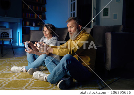 Senior couple sitting on floor and playing video game on console 106295656
