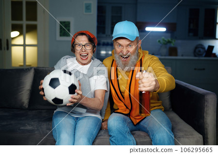Joyful senior family couple watching football game on tv at home Joyful senior family couple watching football game on tv at home 106295665