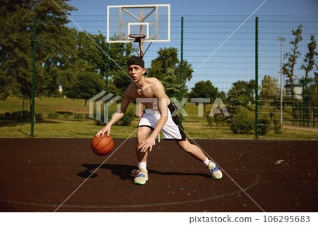 Active teenager basketball player practicing with ball on street court 106295683