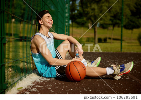 Satisfied teenage basketball player rest sitting on street court 106295691
