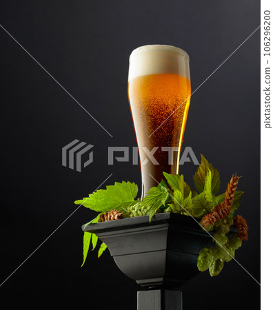 Beer with green hops and wheat ears on a black podium. 106296200
