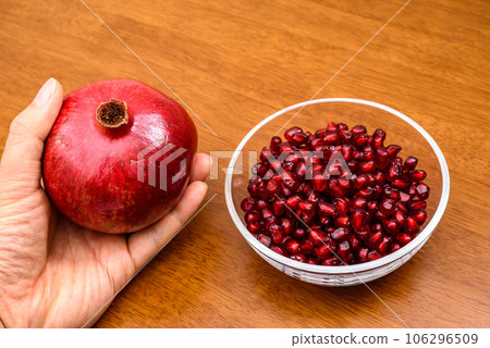 Pomegranate fruit in hand and pomegranate seed coats filled in a bowl Image of wood grain table 106296509
