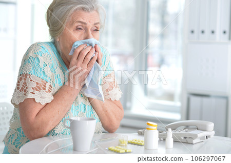 Sad sick senior woman sitting at table with pills at home Sad sick senior woman sitting at table with pills at home 106297067