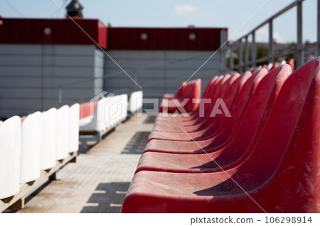 Plastic seats on the grandstand for spectators in the mud. Dirty old red seats in an open-air sports stadium 106298914