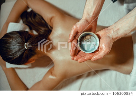 Masseur man holding bowl with warm herb infused oil for back massage 106300884