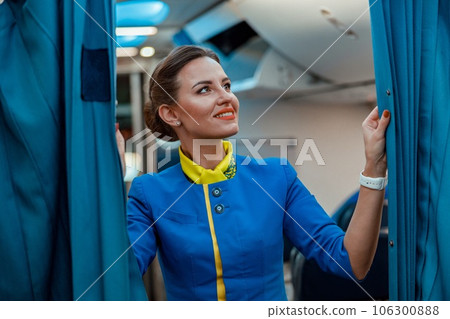 Cheerful woman stewardess holding curtains in airplane 106300888
