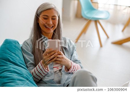 Cheerful woman using mobile phone at home Cheerful woman using mobile phone at home 106300904