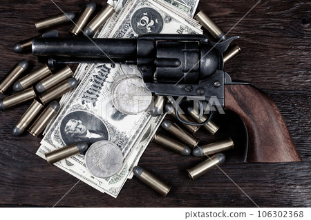 Old west Colt Peacemaker and US banknotes and silver certificates with silver dollar coins and .45 caliber revolver ammunitions 106302368
