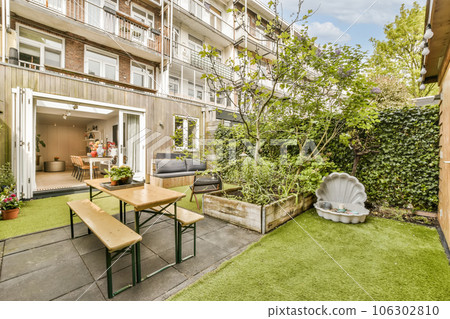 an outdoor living area with green grass and wooden furniture in the back yard is surrounded by plants, shrubs and trees 106302810