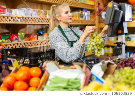 Focused saleswoman weighing grape on scale in grocery store Focused saleswoman weighing grape on scale in grocery store 106303829