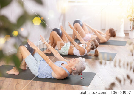 Family grandmother, mother and granddaughter perform fitness exercises lying on floor with softball. 106303907