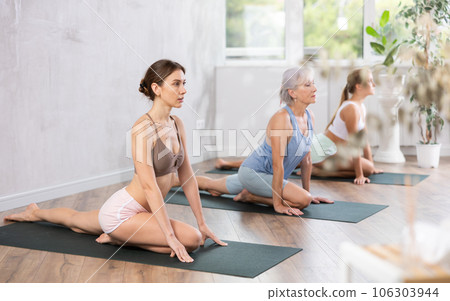 Young woman practicing stretching Half Pigeon Pose during yoga training 106303944