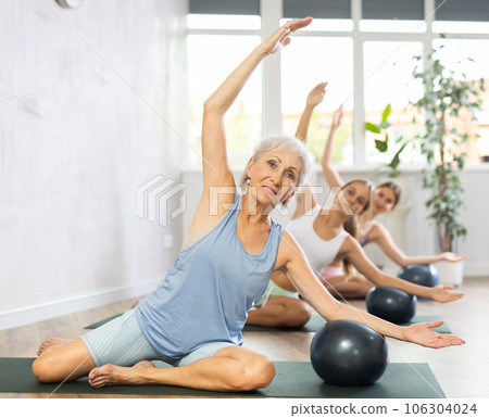 Elderly woman doing pilates with soft ball in group 106304024