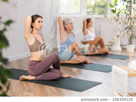 Three generations of women perform sitting Gomukhasana cows head in gym 106304120