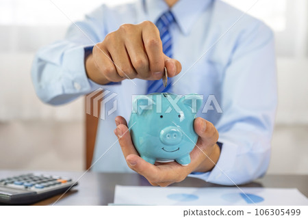 Businessman hand putting coin into blue piggy bank, saving money for future investment plan and retirement fund concept Businessman hand putting coin into blue piggy bank, saving money for future investment plan and retirement fund concept 106305499