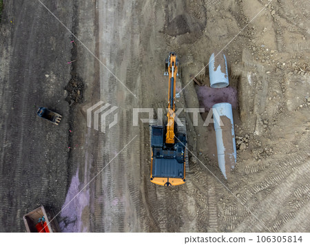Excavator next to an open trench with two culverts ready for a connection juncture.  106305814