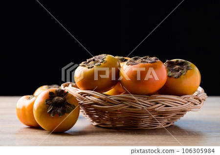 Fresh persimmon fruit in basket on wooden table with black background, Autumn seasonal fruit Fresh persimmon fruit in basket on wooden table with black background, Autumn seasonal fruit 106305984