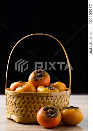 Fresh persimmon fruit in basket on wooden table with black background, Autumn seasonal fruit 106305987