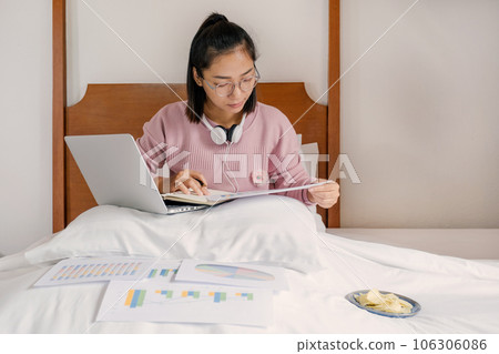 businesswoman holding pen used laptop video conferences and eating snack on the bed, healthy food and work from home concept businesswoman holding pen used laptop video conferences and eating snack on the bed, healthy food and work from home concept 106306086