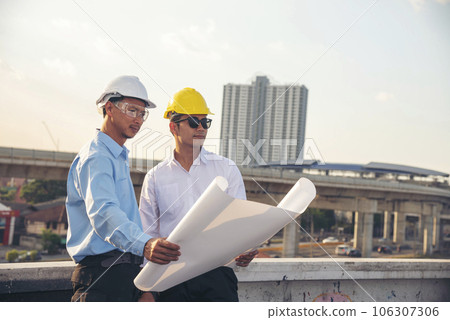 Two men engineer look at blueprint architecture building contractor design in modern city development. Males engineer holding project planing partner teamwork. Man meeting together construction site Two men engineer look at blueprint architecture building contractor design in modern city development. Males engineer holding project planing partner teamwork. Man meeting together construction site 106307306