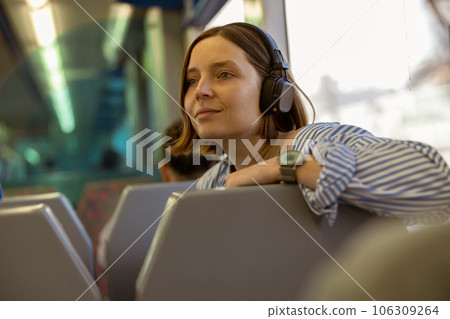 Young smiling woman listen music in headphones while traveling in public transport  106309264